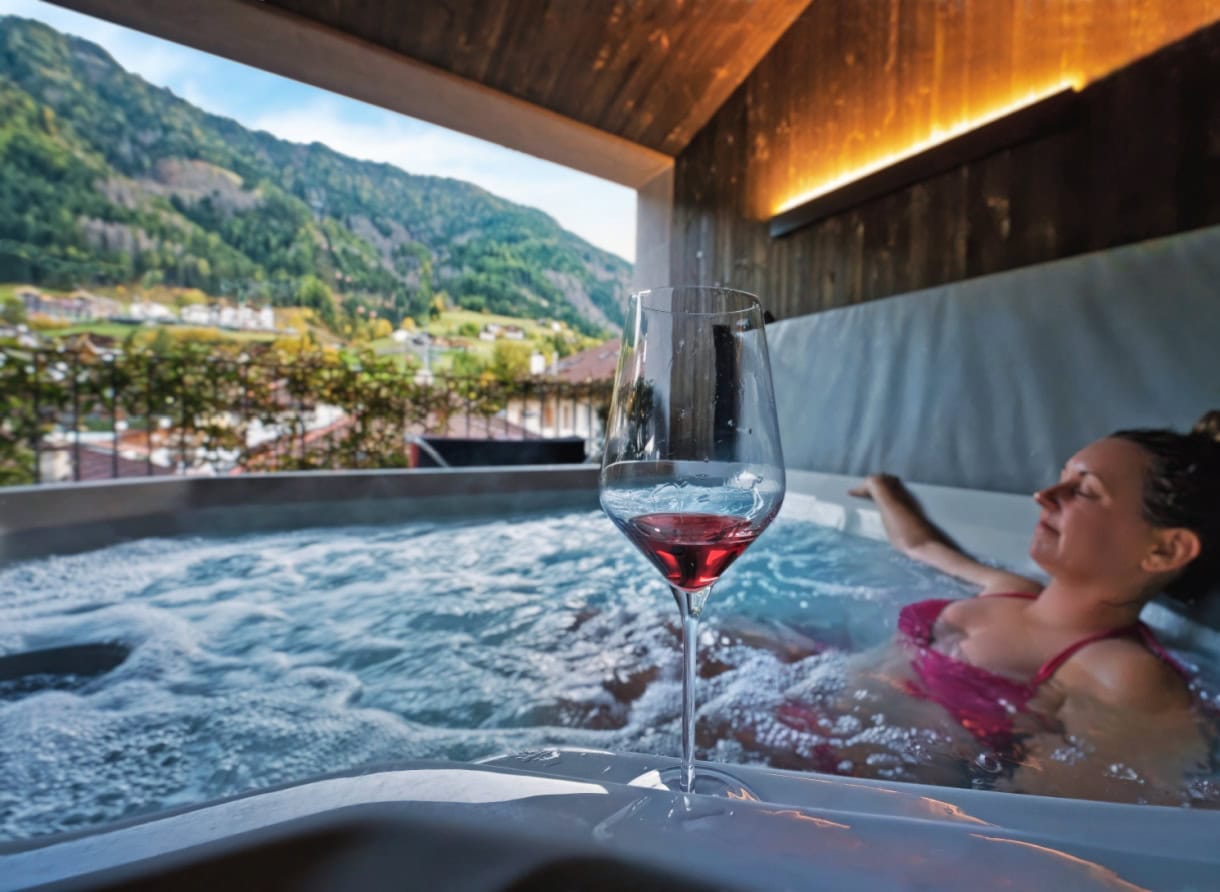 Aquila Dolomites Residence: Ortisei Below, the Dolomites Beyond, and You in Between 10 A woman sitting in a hot tub enjoying a glass of red wine at Aquila Dolomites Residence in Ortisei.