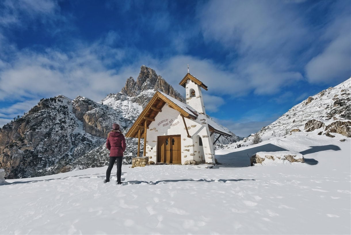 A woman taking in the simple beauty of Cappella della Visitazione at Passo Falzarego — a mountain‑top chapel nestled beneath the slopes of Lagazuoi near Cortina d' Ampezzo.