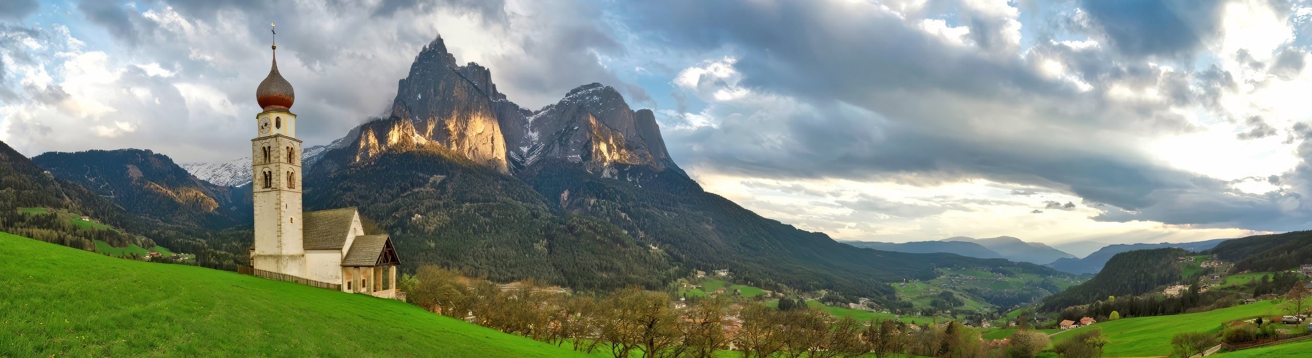 A view of the St. Valentin Church in Alpe di Siusi with the sun lighting the face of Mt. Schlern.