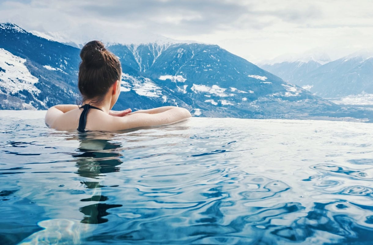 A woman sitting in an infinity pool overlooking South tyrol in the winter.