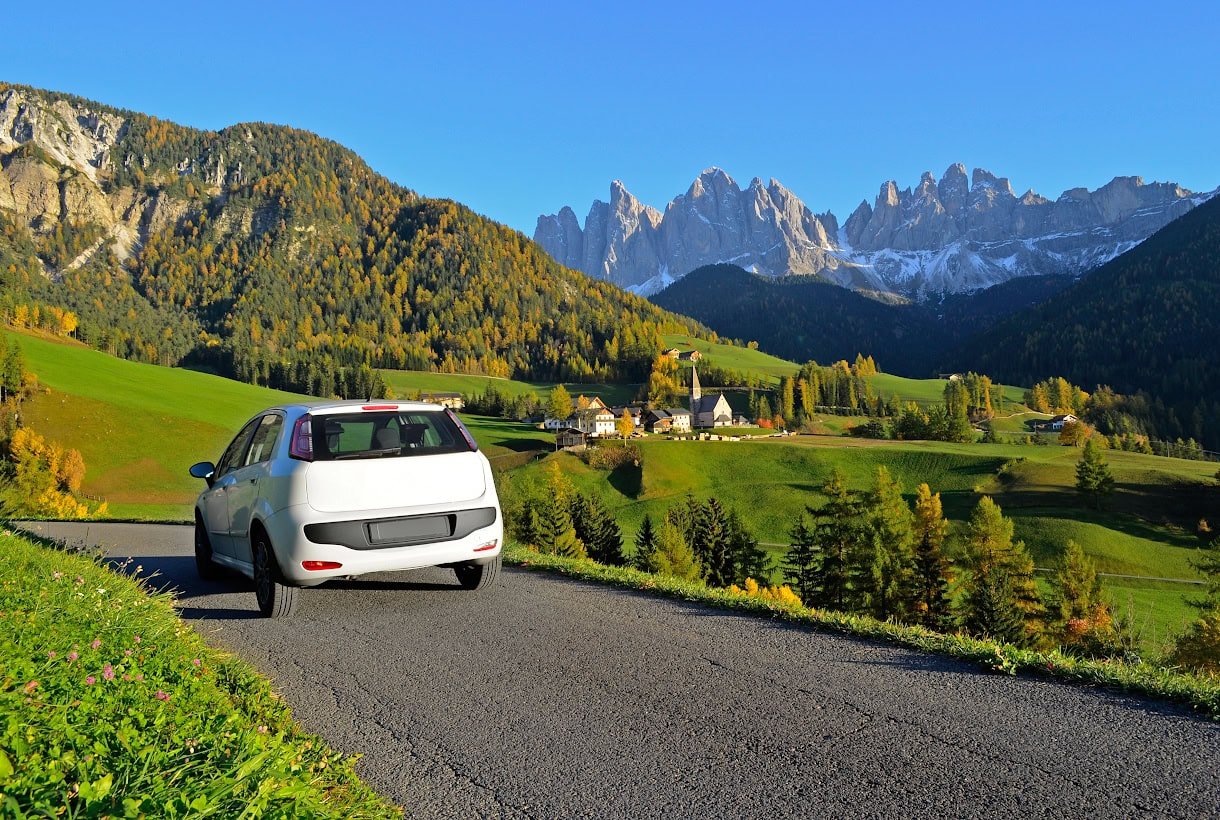 A rental car sitting in front of the Dolomites in Val di Funes in fall.
