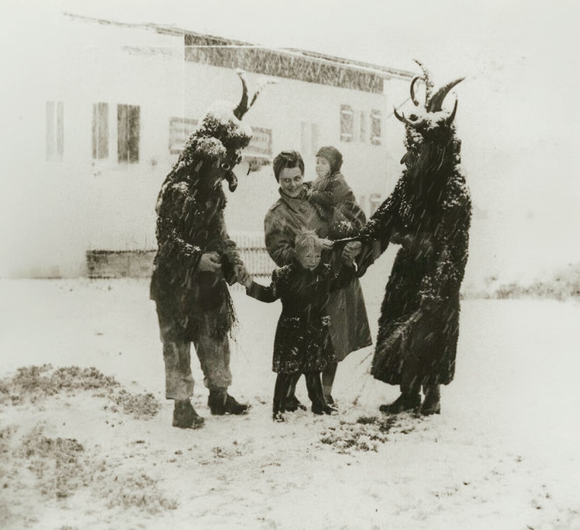Vintage photograph of two Krampus frightening a crying child in the snow in Austria.