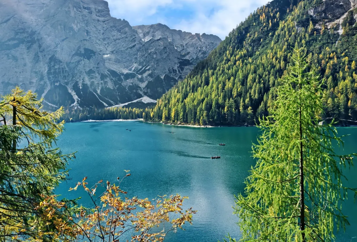 Beyond the Peaks: 12 Must-See Lakes in South Tyrol and the Dolomites 4 Lago di Braies in autumn with golden larches, turquoise water and small rowboats leaving wakes beneath the Croda del Becco cliffs.
