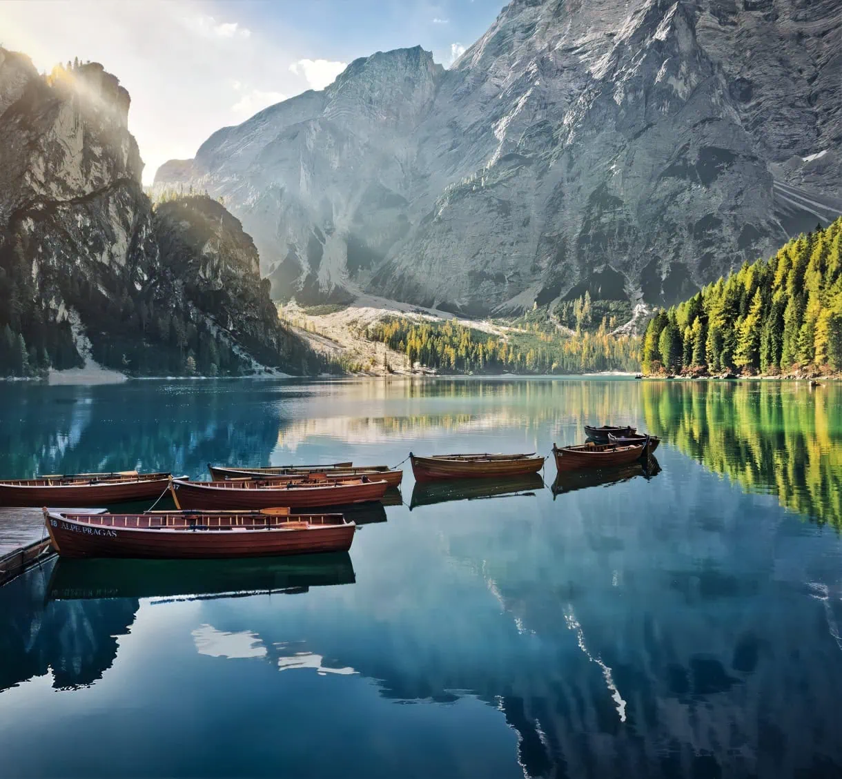 Beyond the Peaks: 12 Must-See Lakes in South Tyrol and the Dolomites 3 Lago di Braies in autumn with the morning sun spilling over the cliffs and small rowboats floating in the turquoise water.
