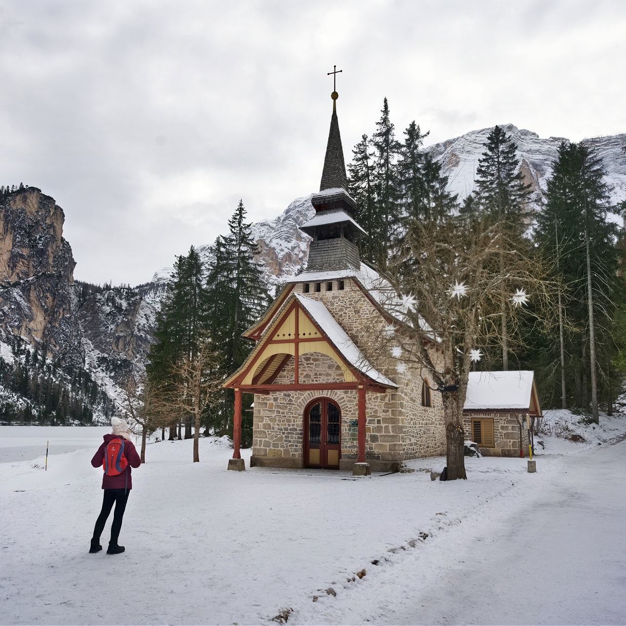 A chapel and a girl hiker along the shore of Lago di Braies in the winter. 