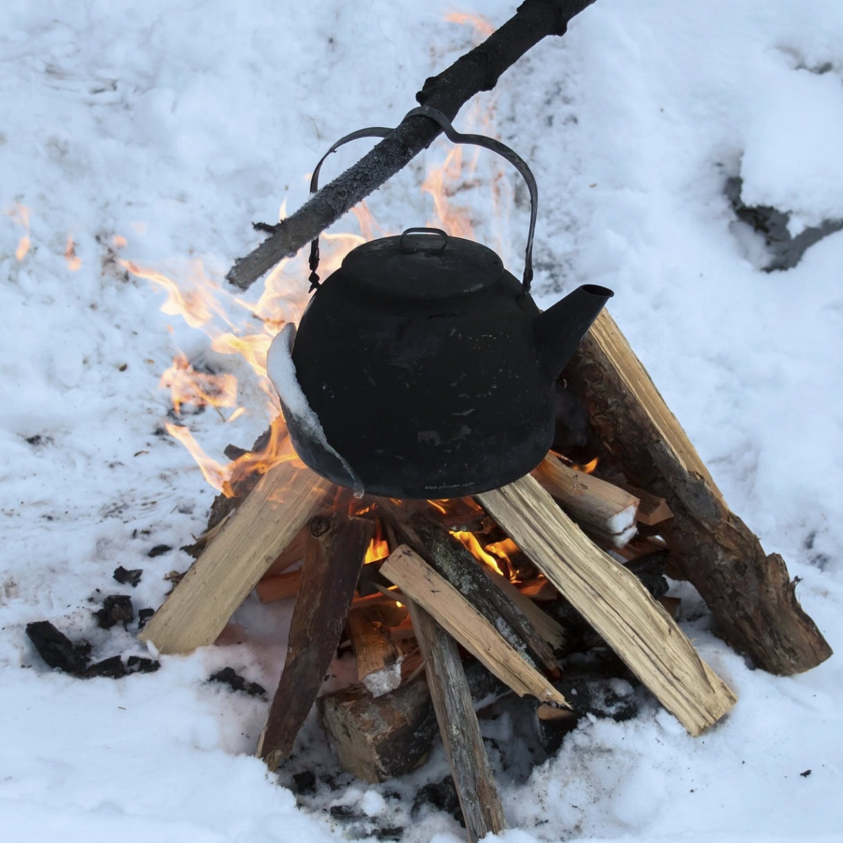 A winter campfire with a black pot above the flames. 