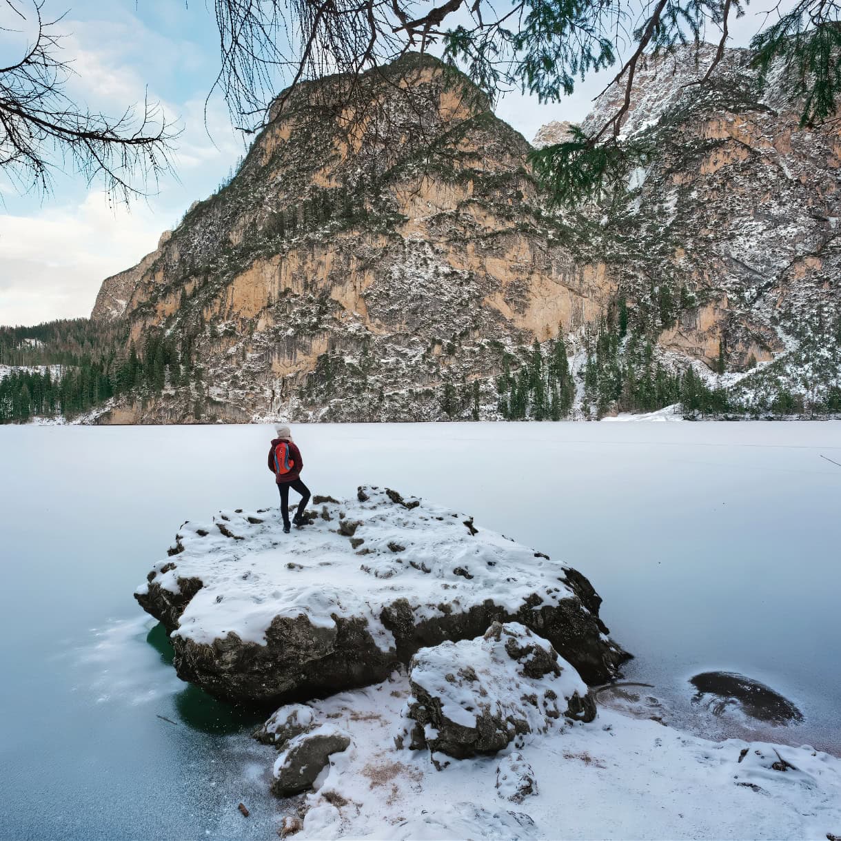 A girl hiker looking at a frozen Lago di Braies in the Dolomites in winter.