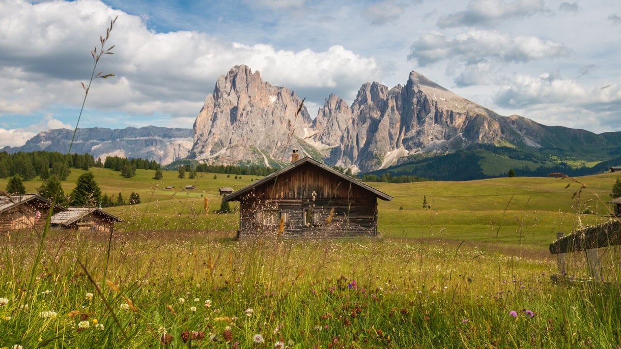 A wooden hut in the middle of Alpe di Siusi with the Sassolungo massif in the backdrop.