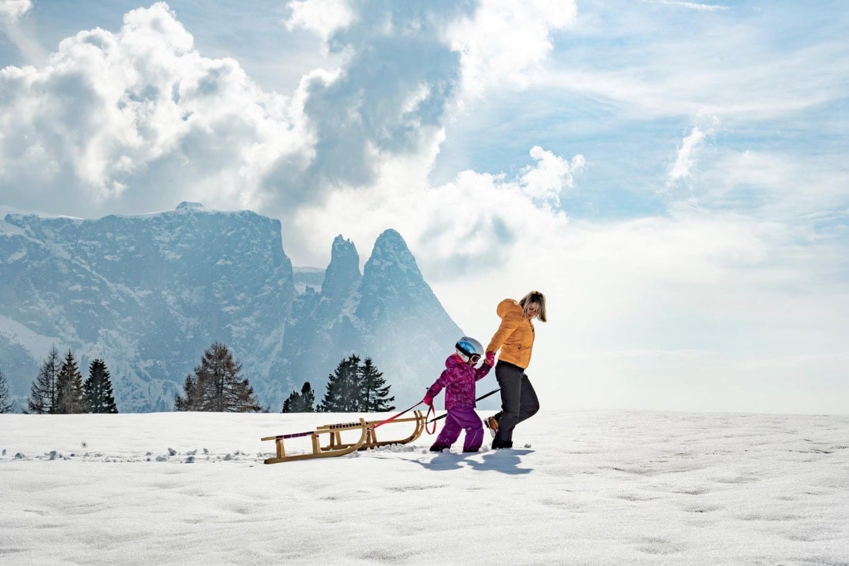 A mother and child tobogganing in the Dolomites in winter.