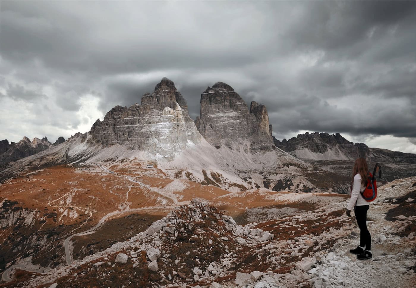A female hiker looking back at Tre Cime di Lavaredo while doing the Cadini di Misurina hike. on a cloudy day in the Dolomites.
