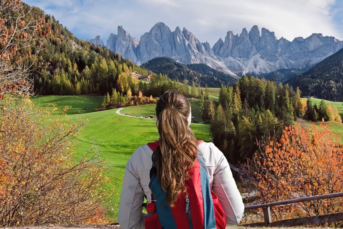 A female hiker looking the famous church scene in Val di Funes in the Dolomites during autumn.