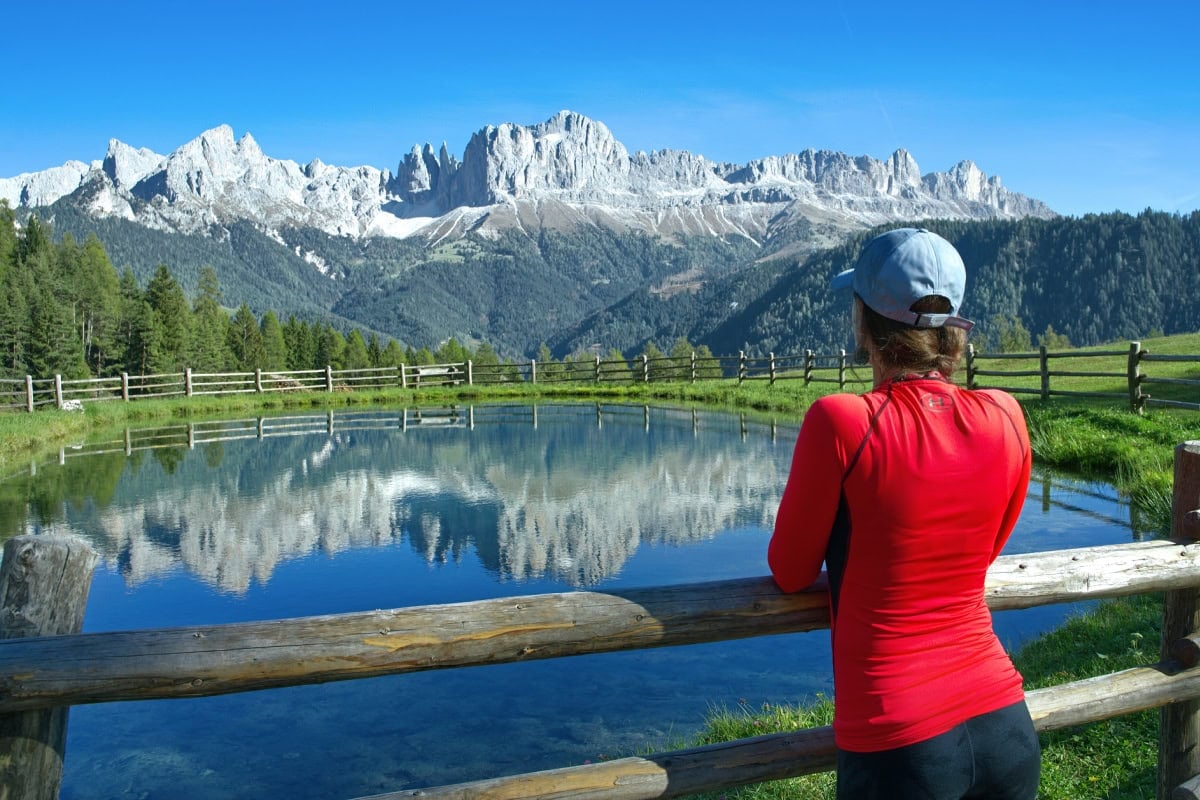 A hiker overlooking a glass still pond at the Rosengarten Group in the Dolomites.